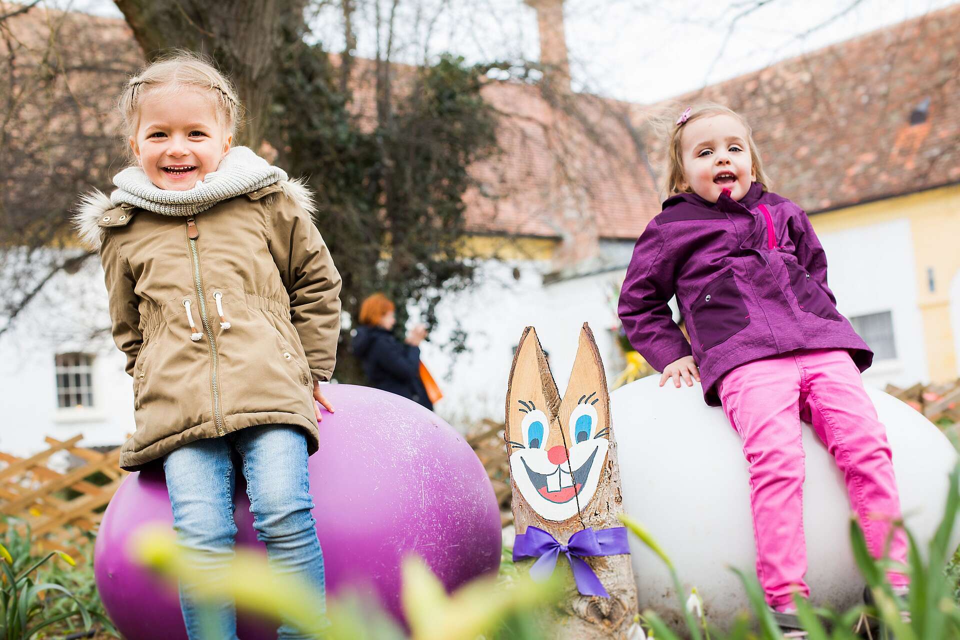 Zwei kleine Mädchen sitzen auf großen, bunten Ostereiern