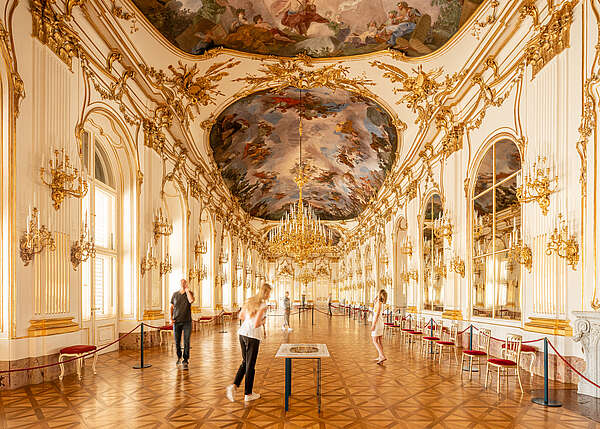 View of the Great Gallery, people looking at the ceiling frescoes, golden chandeliers hanging from the ceiling in the center