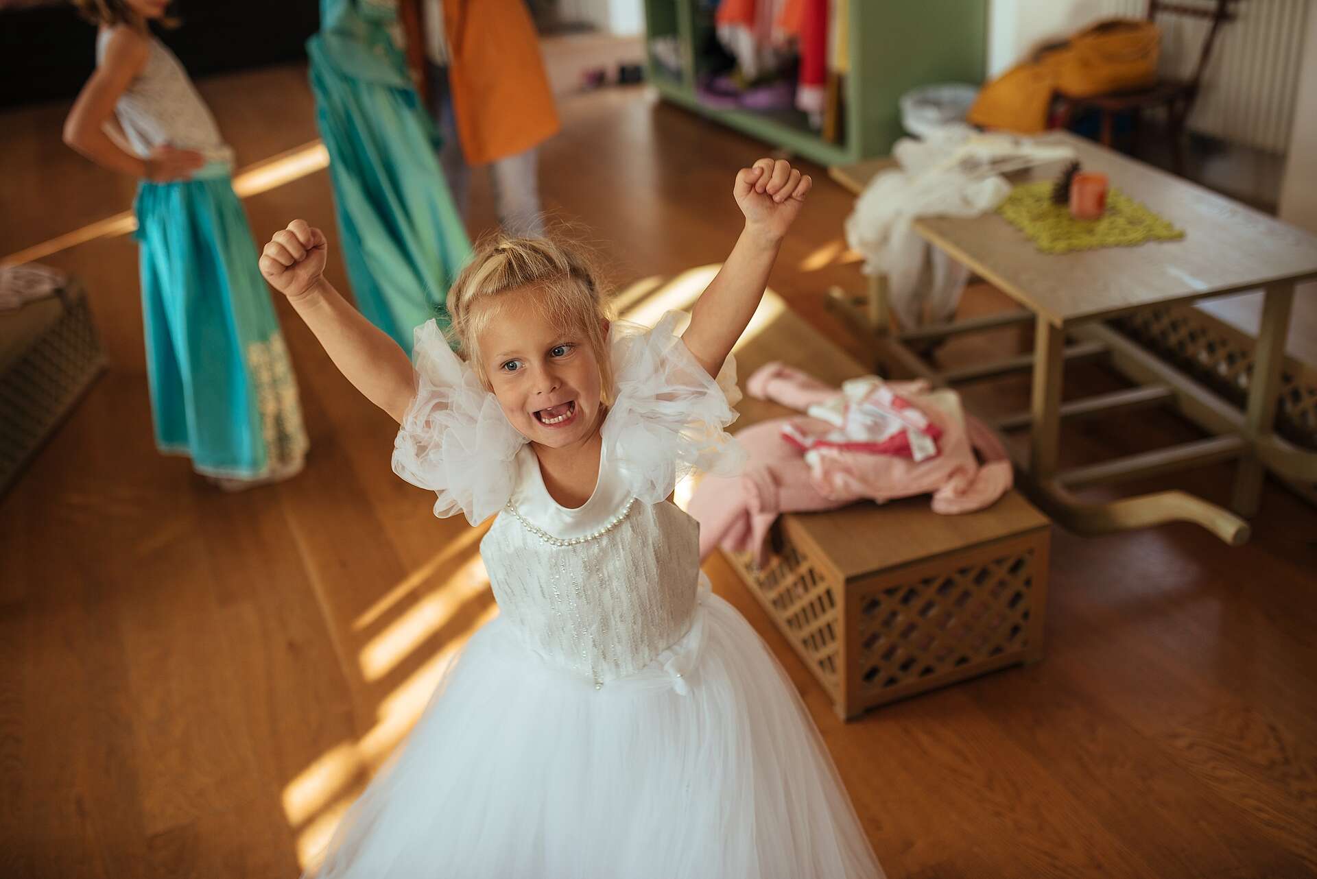 Kleines blondes Mädchen in weißem Kleid freut sich und hält die Arme in die Höhe