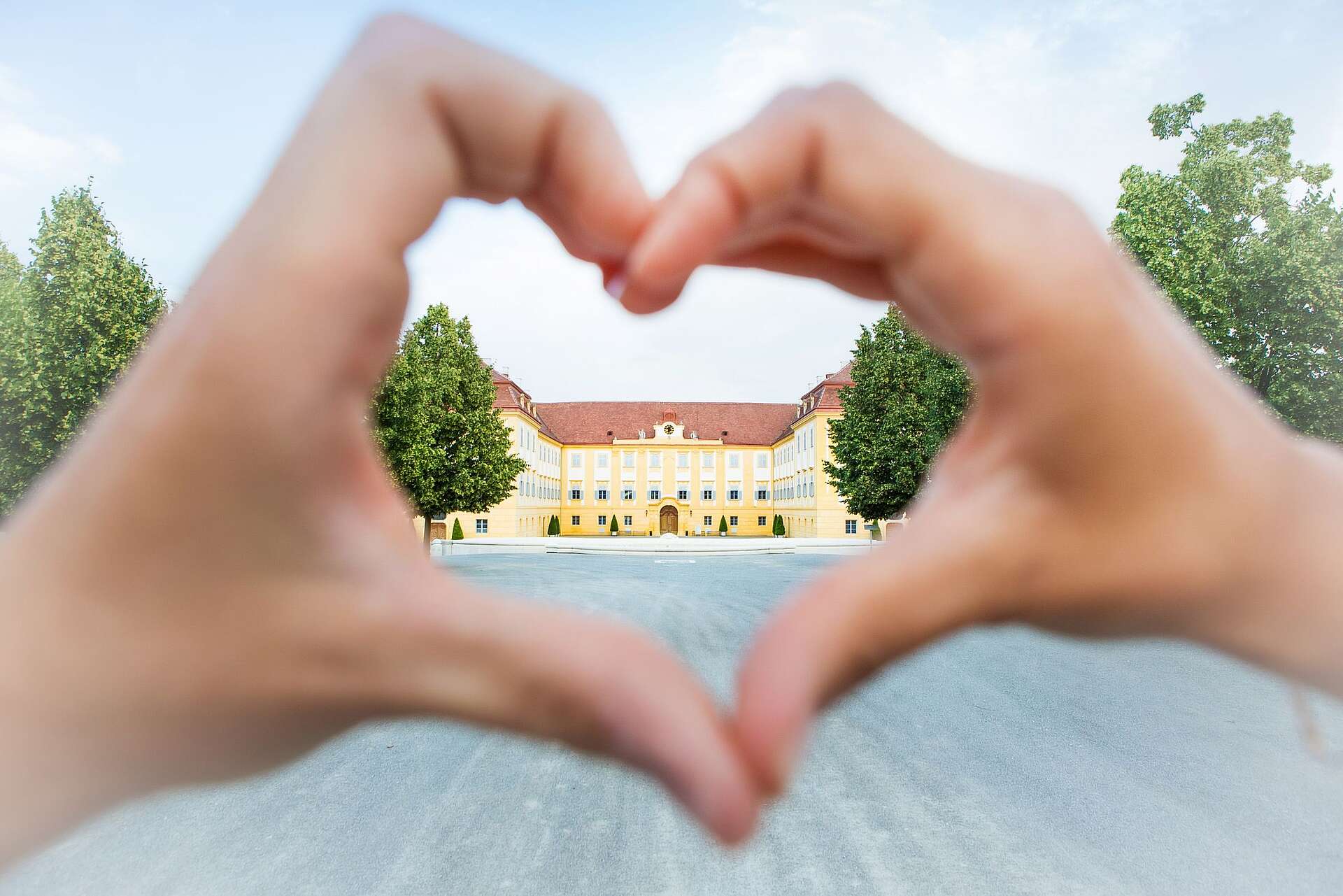 Hände in Form von Herzen, im Hintergrund sieht man Schloss Hof