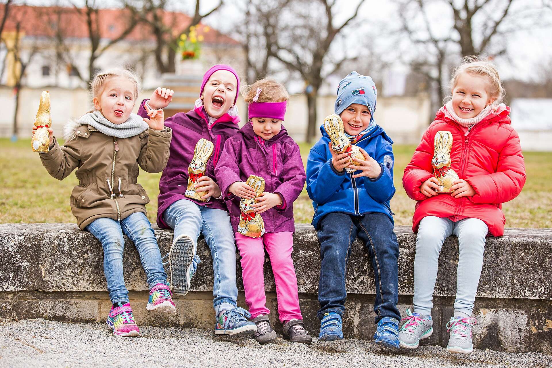 Fünf Kinder sitzen auf einer Mauer und halten Schokoosterhasen in der Hand