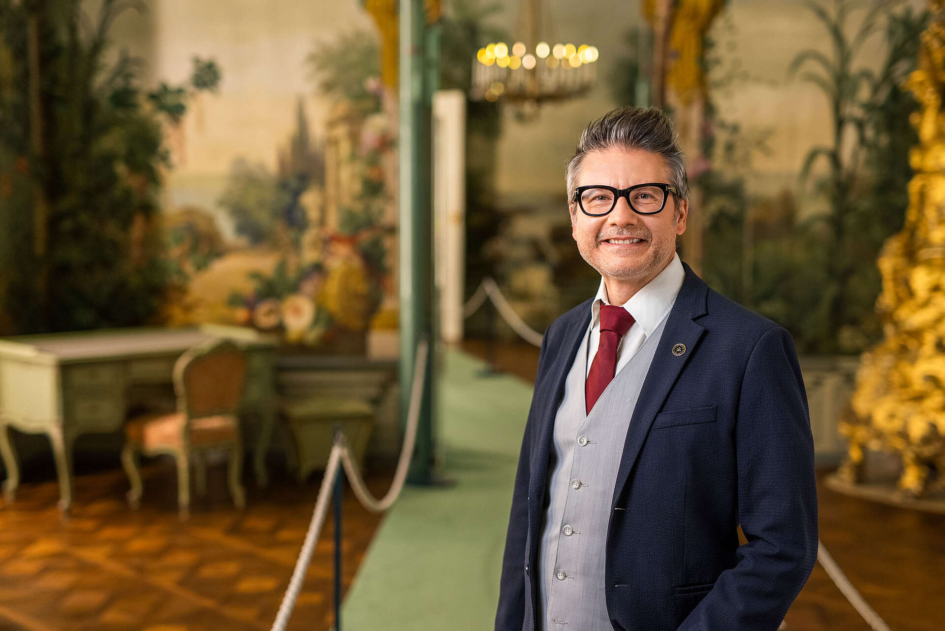 Mann steht im Berglzimmer und lächelt in die Kamera