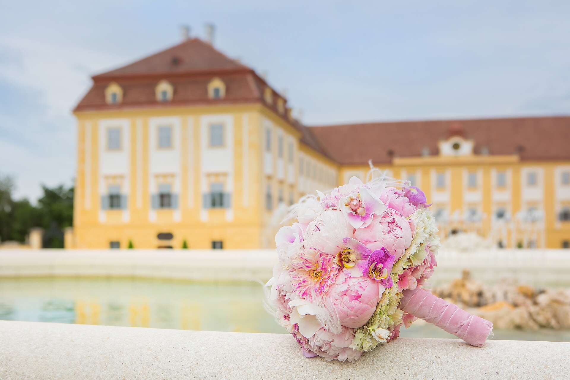 Hochzeitsstrauß liegt auf Brunnenrand mit Schloss Hof im Hintergrund