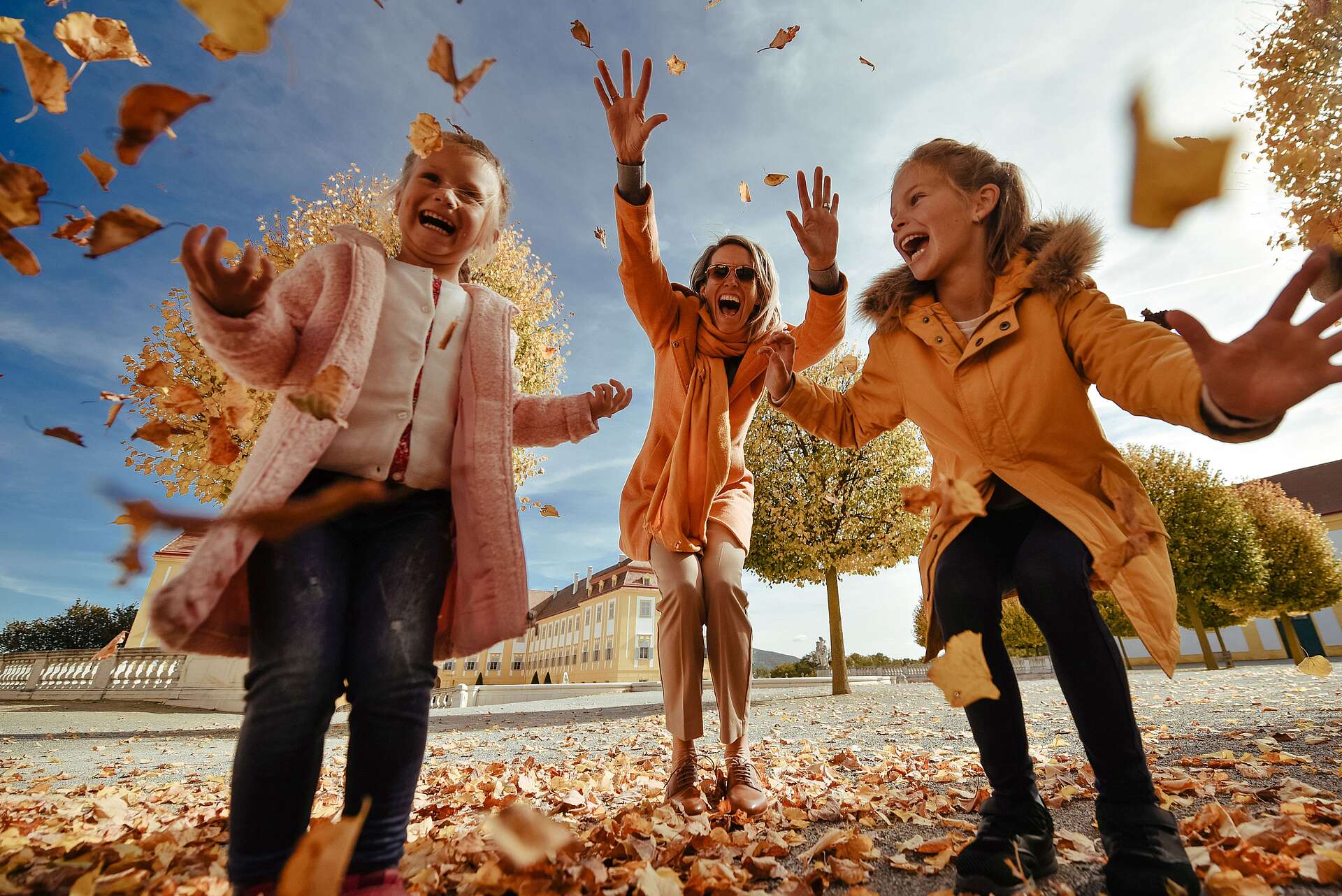 Mutter und zwei Kinder wirbeln Blätter in die Luft und lachen fröhlich